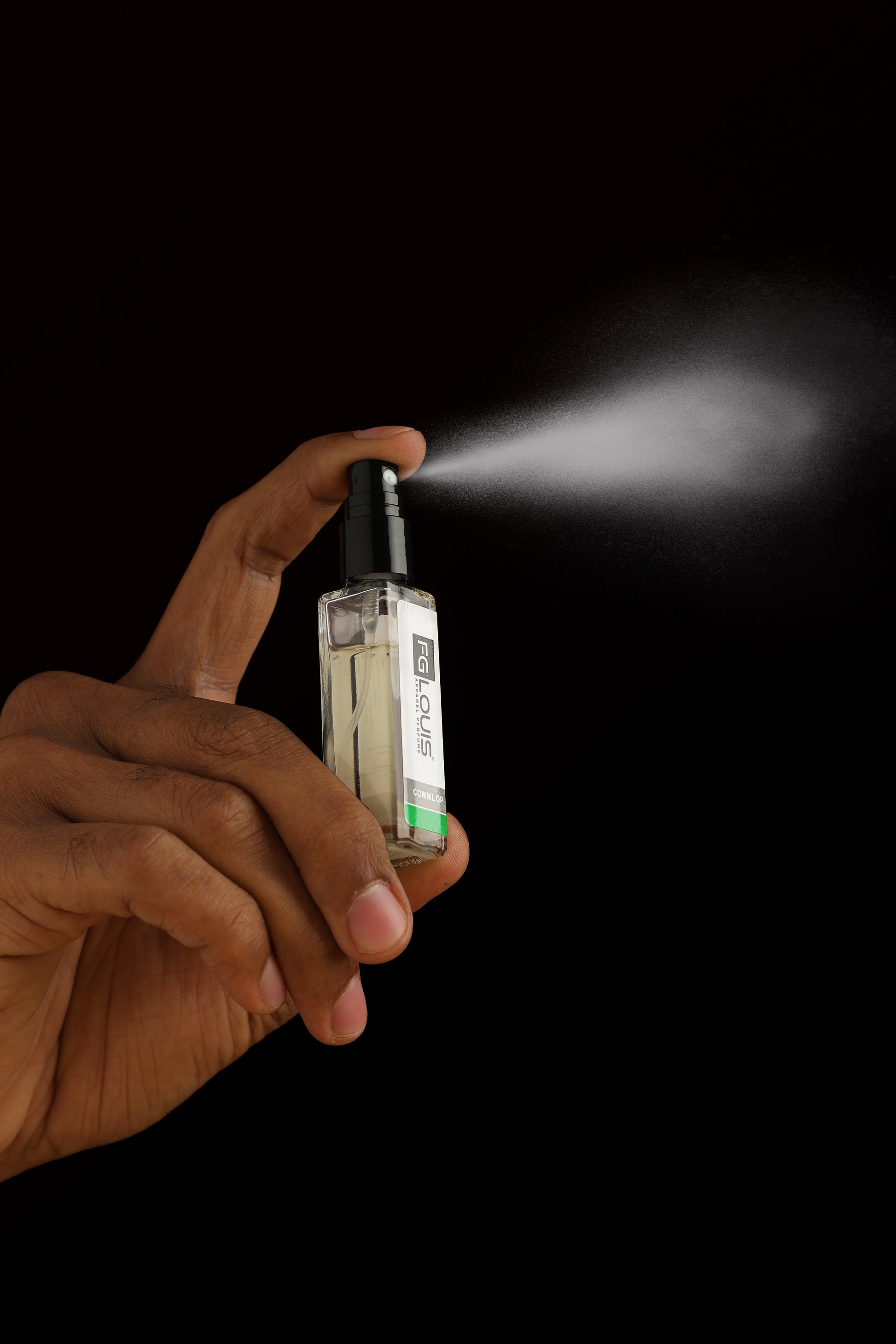 Hand holding a small spray bottle with mist against a black background
